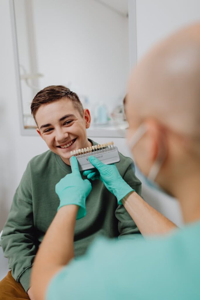 A Boy Smiling while a Person Wearing Latex Gloves is Holding a Dental Shade Guide